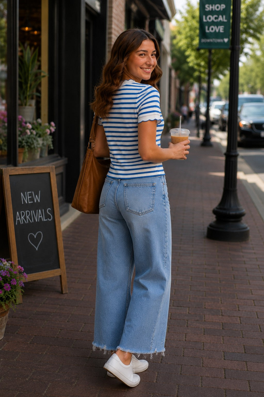 Back and side view of model wearing a blue and white striped scalloped short sleeve knit top with light wash cropped wide leg jeans while walking through a charming downtown shopping district.